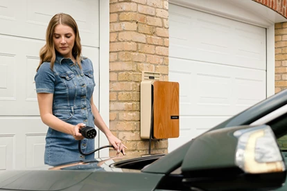 Woman holding an electric vehicle charger next to a green car.
